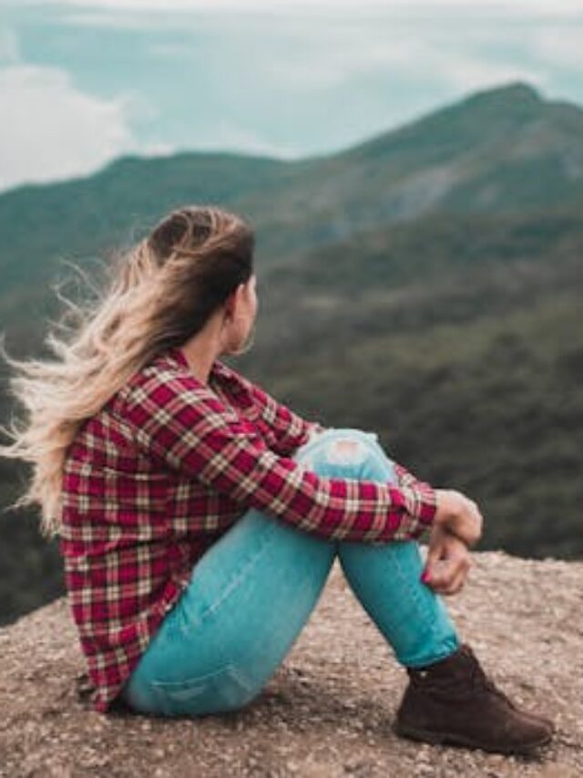 Side View Photo of Woman Sitting on Ground Overlooking a Hill